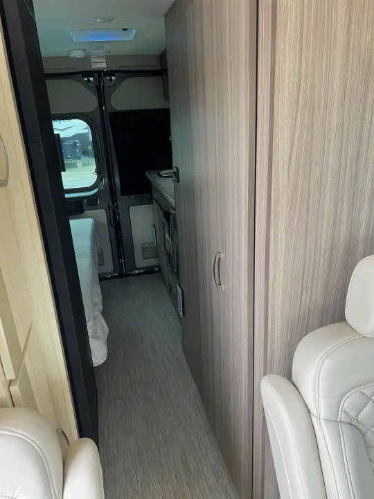 Inside a modern **rv rental**, looking towards the rear. Features a light-toned interior with a bed, galley, & captains chair.. Jayco Swift Li 2023