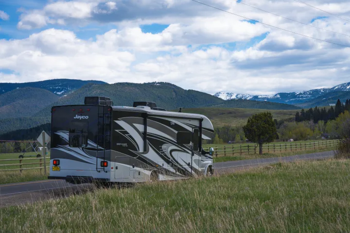 Jayco Greyhawk RV rental on a scenic road through mountains with a cloudy sky and green fields.. Jayco Greyhawk Prestige 2021