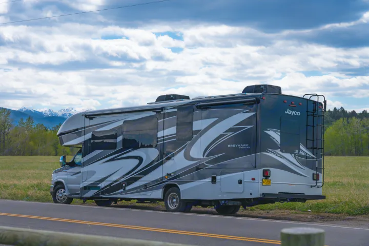 This sleek Jayco rv rental, with its unique grey design, rests roadside against a backdrop of mountains & a cloudy sky.. Jayco Greyhawk Prestige 2021