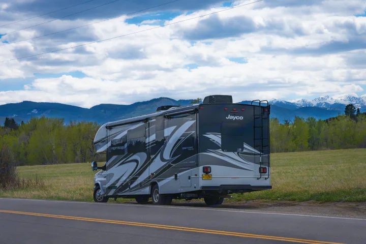 Experience nature with this Greyhawk rv rental. A gray Jayco motorhome overlooks mountains & fields under a cloudy sky.. Jayco Greyhawk Prestige 2021