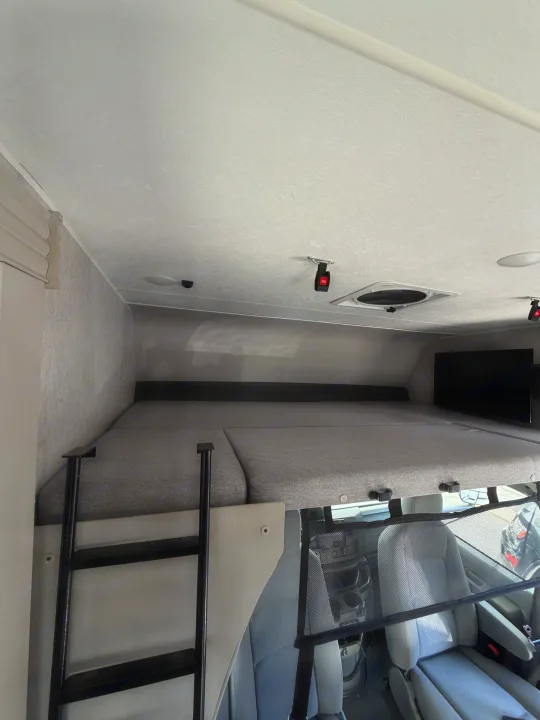 View inside an RV rental: gray cab-over bunk bed with ladder, safety net, TV, and driver's area below.. Forest River Coachmen Freelander 2023