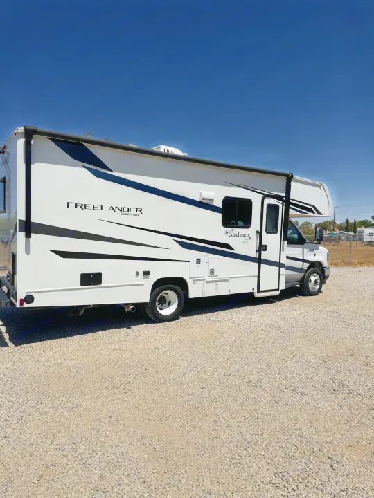 This white Coachmen Freelander Class C motorhome, an ideal RV rental, is parked on a gravel lot under a clear blue sky.. Forest River Coachmen Freelander 2023