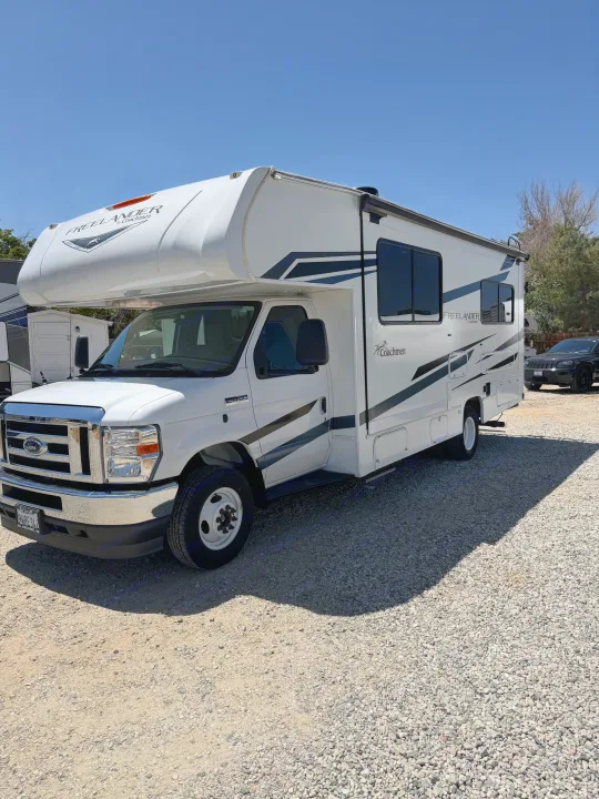 A white Coachmen Freelander Class C RV rental parked on a sunny gravel lot under a clear blue sky.. Forest River Coachmen Freelander 2023