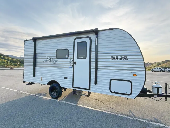 This white and grey Jay Flight SLX Sport Edition travel trailer RV rental is parked, ready for your next adventure. Hills in background.. Jayco 1UJBC0AJ6F7750334 2026