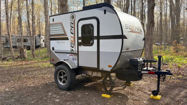 A Geo Pro travel trailer, ideal for an rv rental, parked in a wooded campsite with stabilization jacks visible.. Forest River Rockwood Geo Pro 2018