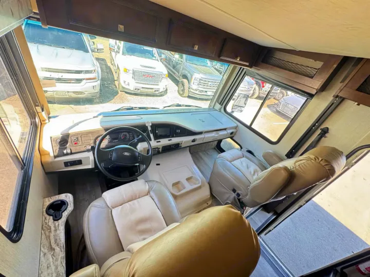 RV rental cockpit view. Tan driver/passenger seats, Ford steering wheel, dashboard, and view of parked vehicles outside.. Holiday Rambler Admiral 2019
