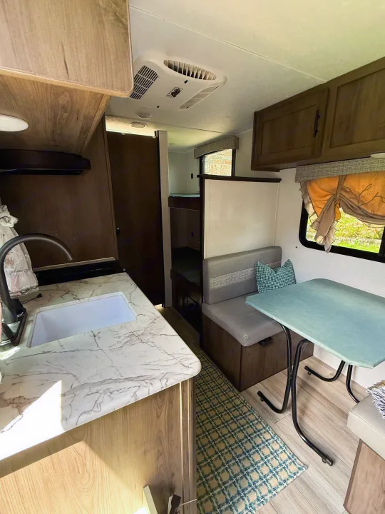 Cozy rv rental interior featuring a kitchen with marble-look counter, dining booth, window with curtain, AC unit, & bunk beds.. Coachmen 17BH 2022