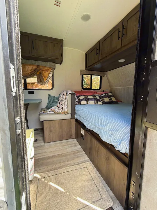 RV rental interior: cozy bed with blue stripes, plaid pillows, bench seating, and wooden cabinets in a compact space.. Coachmen 17BH 2022