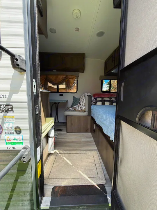 Step into this inviting rv rental! Interior view of a travel trailer with a bed, dinette, and fire extinguisher for safe camping.. Coachmen 17BH 2022