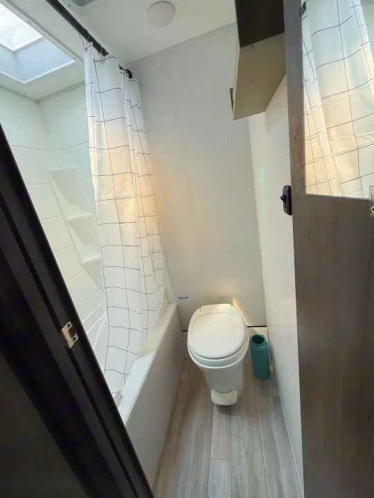 Clean RV rental bathroom with a compact shower/tub, toilet, and grid-patterned curtain, ready for your adventure.. Coachmen 17BH 2022