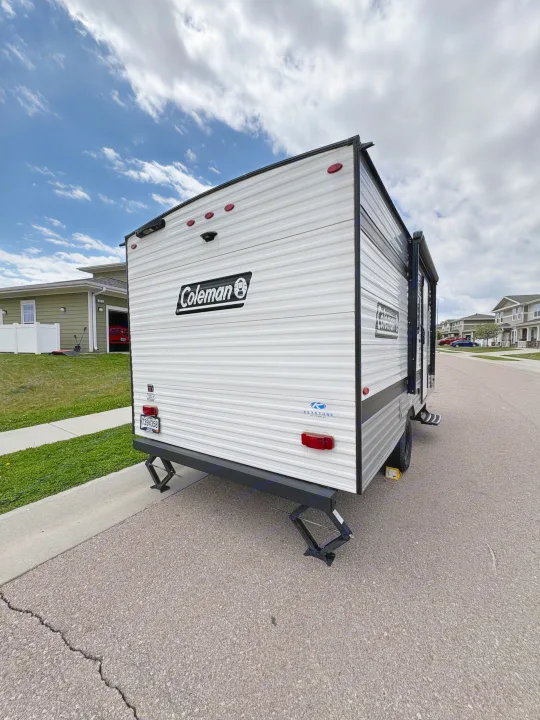 Coleman travel trailer (RV rental) parked on a residential street. White and black exterior with extended stabilizer jacks.. Keystone RV Coleman 2025