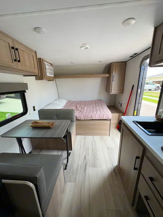 Modern RV rental interior with a comfortable bed, dinette, and compact kitchen. Light-filled living space ready for travel.. Keystone RV Coleman 2025