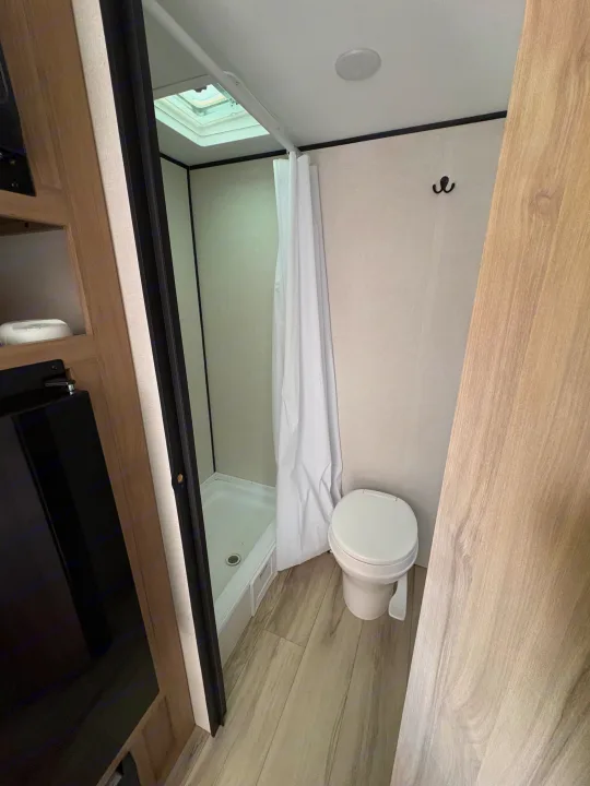 This RV rental bathroom features a compact shower with skylight, toilet, and modern light wood flooring. Essential for road trips.. Keystone RV Coleman 2025
