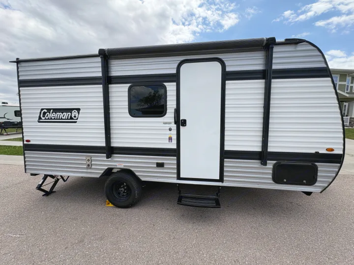 Silver Coleman travel trailer with black awning and steps, parked on asphalt. Ideal for an RV rental adventure.. Keystone RV Coleman 2025
