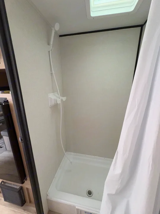 RV rental: Compact white shower stall with handheld shower, controls, drain, white curtain, and ceiling skylight.. Keystone RV Coleman 2025