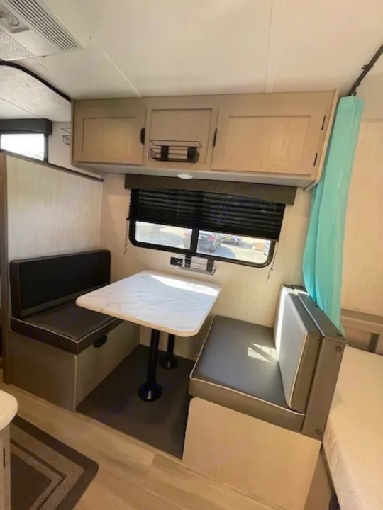 RV rental dinette featuring cushioned benches, a white table, overhead cabinets, and a large window for natural light.. Coachmen Clipper 2025