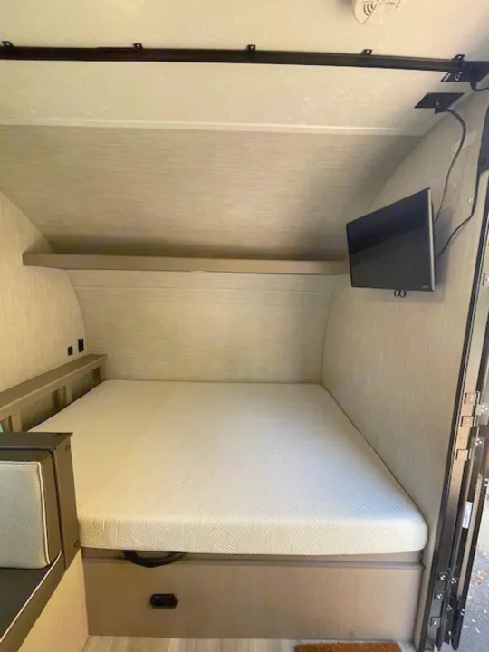 An RV rental's cozy bedroom, featuring a white mattress, wall-mounted TV, and built-in storage.. Coachmen Clipper 2025