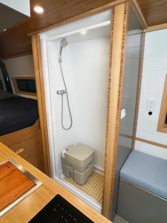 Experience a compact **rv rental** interior with a modern shower, portable toilet, cozy bed, and functional kitchen space.. Mercedes-Benz Sprinter 2024