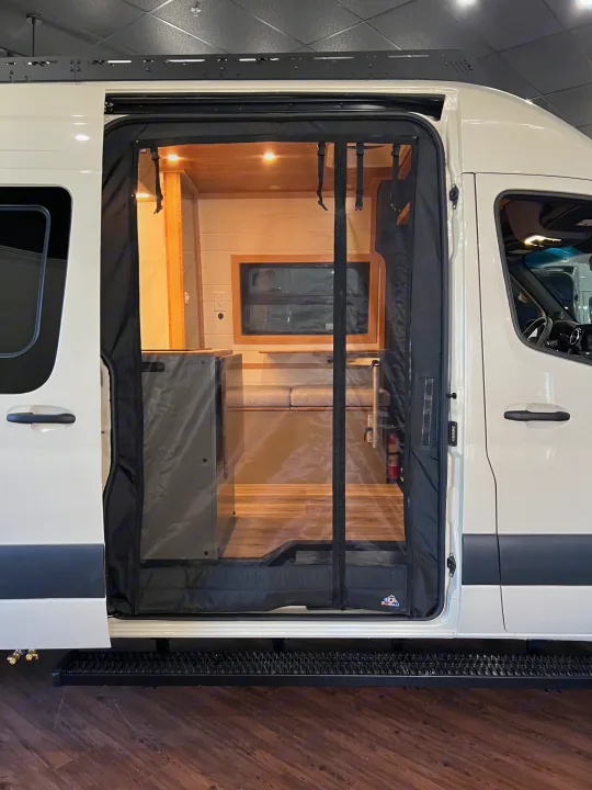 Open side door of an RV rental camper van, with a mesh screen revealing its functional and warm wooden interior.. Mercedes-Benz Sprinter 2024