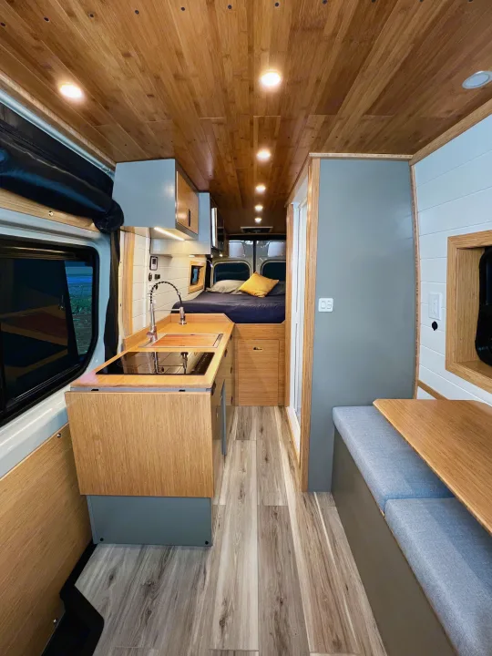 Modern camper van RV rental interior: kitchen, dinette, and bed area with bamboo finishes and light wood flooring.. Mercedes-Benz Sprinter 2024