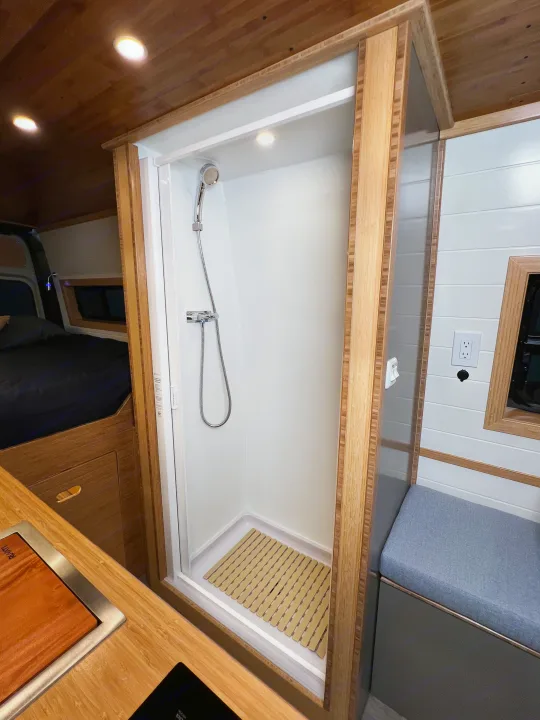 Modern rv rental interior with compact shower, cozy sleeping area, and stylish wood accents. Ideal for camper van adventures.. Mercedes-Benz Sprinter 2024