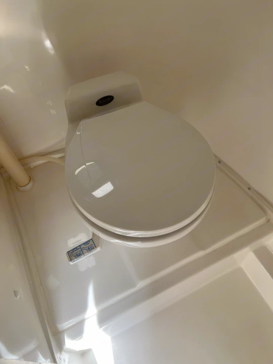 White Traveler RV rental toilet with lid closed. Visible flush instructions (lift to add water, press to flush) are on the base.. Casita Casita Trailer 2000