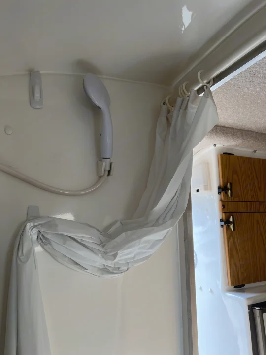RV rental shower: white shower head, hose, and curtain secured by Command hooks. Features white walls and adjacent wooden cabinets.. Casita Casita Trailer 2000