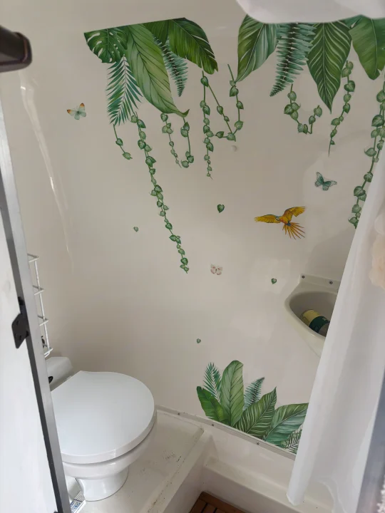 RV rental bathroom with tropical leaf, butterfly, and parrot decals. Features a white toilet, compact sink, and shower area.. Casita Casita Trailer 2000
