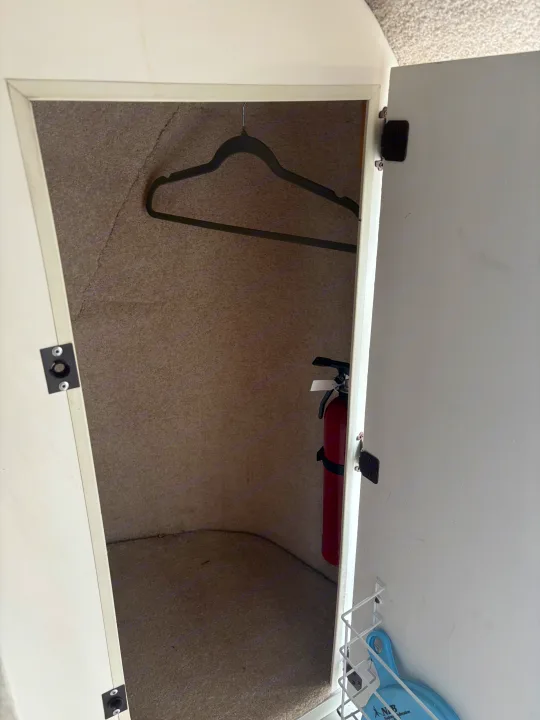 RV rental storage cabinet with a fire extinguisher, clothes hanger, and a white wire shelf on the door.. Casita Casita Trailer 2000
