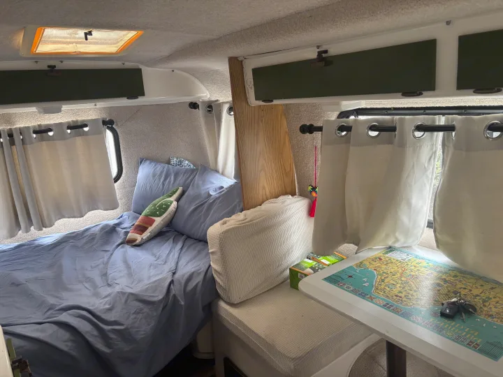 Inside a compact rv rental: a comfy bed, small dinette with a map, overhead storage, and light curtains.. Casita Casita Trailer 2000
