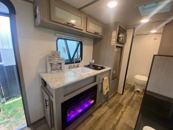 RV rental interior features a kitchen with sink, stove, microwave, & electric fireplace. Bathroom & entry door are also visible.. Dutchmen Coleman 2024