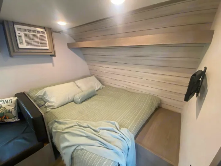Inside an RV rental, discover this compact bedroom with a comfy bed, air conditioning, and wall-mounted TV bracket.. Dutchmen Coleman 2024