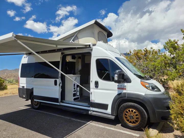 White pop-top rv rental camper van with extended awning parked outdoors, revealing open door and interior. Ready for adventure!. Thor Tellaro 2022