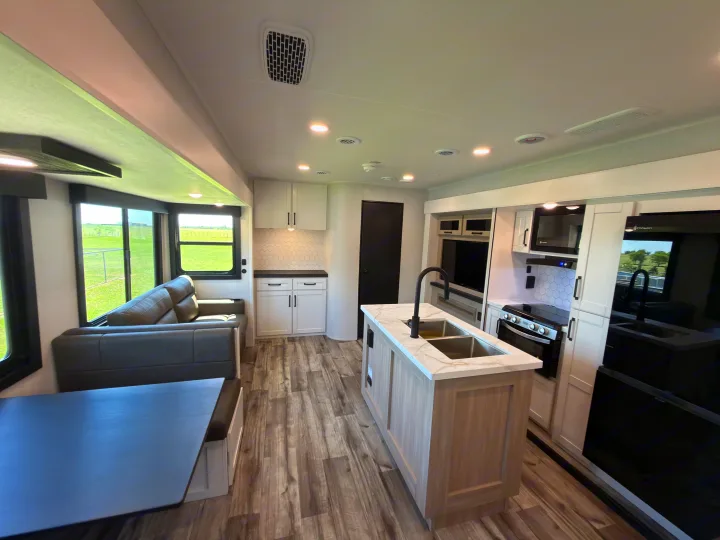 Modern rv rental interior: full kitchen with island, living area, and dinette. Light wood-look floors & white cabinetry.. Highland Ridge RV Open Range Roamer 2026