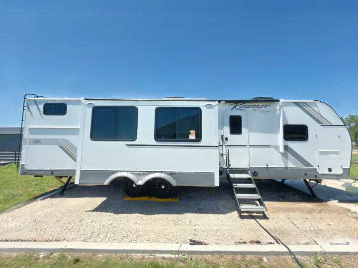 White Roamer Open Range travel trailer (RV rental) parked on a sunny gravel campsite with steps extended.. Highland Ridge RV Open Range Roamer 2026