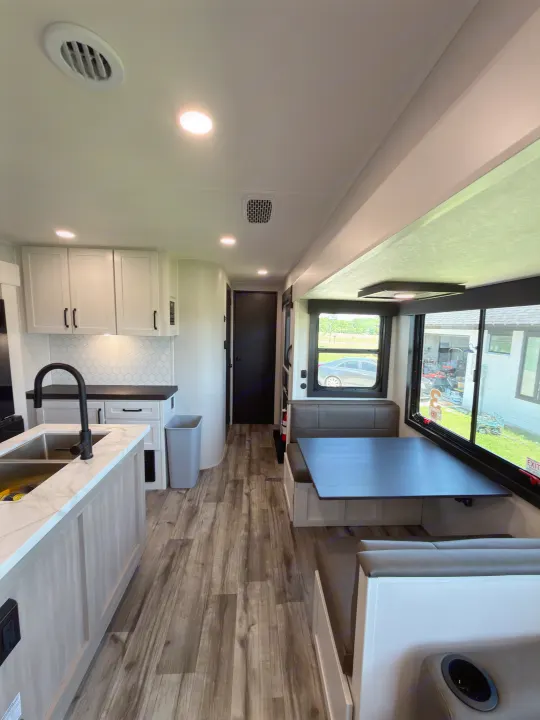 Spacious rv rental interior featuring a bright kitchen island with a sink, white cabinets, and a comfortable dining booth.. Highland Ridge RV Open Range Roamer 2026