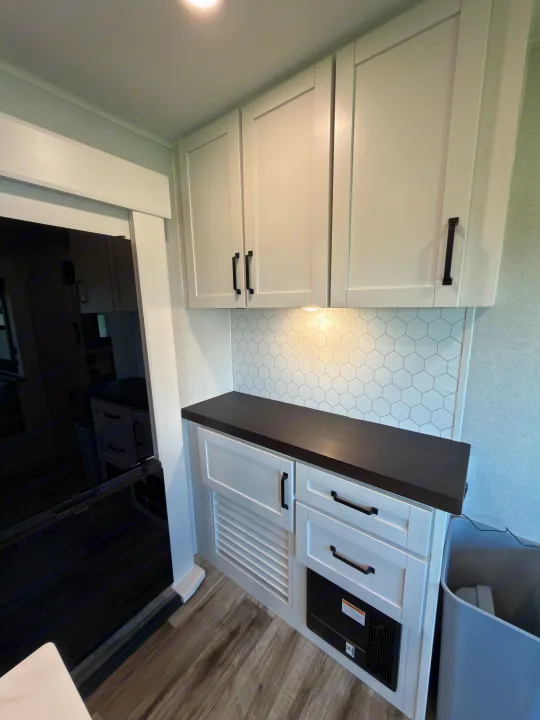 Clean & modern rv rental kitchen area features white shaker cabinets, dark counter, hexagon backsplash, and under-cabinet light.. Highland Ridge RV Open Range Roamer 2026
