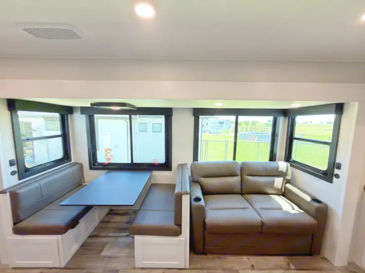 Inside this RV rental: a modern dinette with dark benches, a reclining sofa with cupholders, and bright windows with outdoor views.. Highland Ridge RV Open Range Roamer 2026
