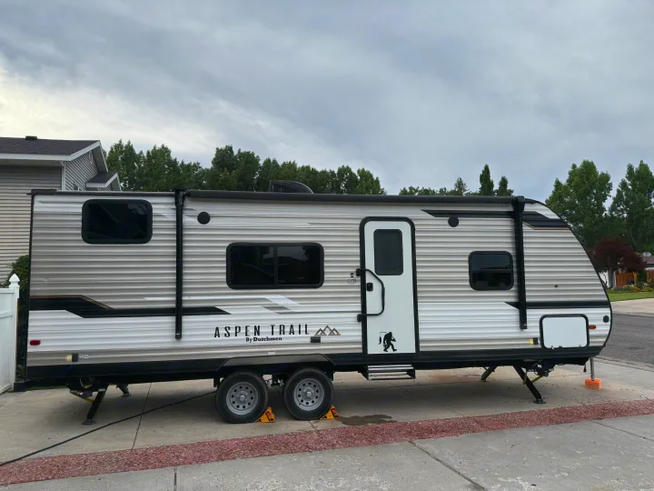 Aspen Trail travel trailer rv rental, detailed with a Bigfoot decal, parked on a driveway under an overcast sky. Ready for your outdoor trip!. Aspen Trail Aspen Trail Trailer 2021