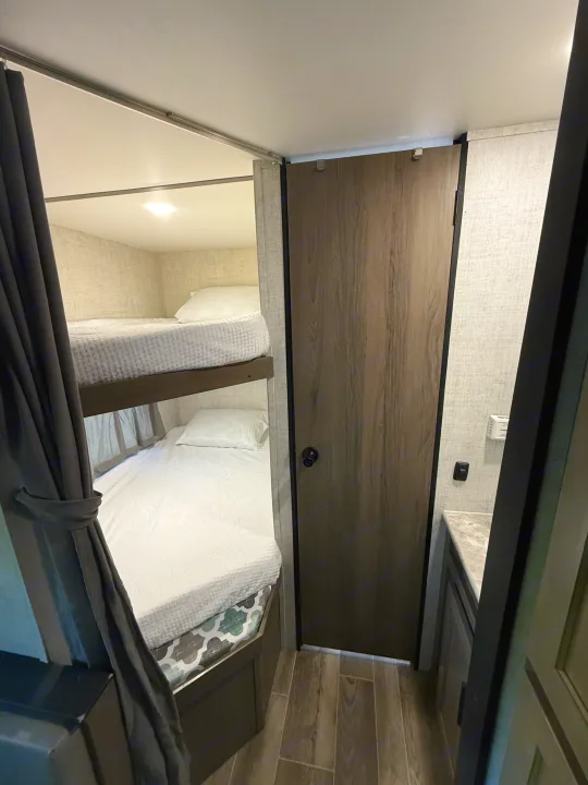 RV rental interior offering bunk beds with soft white bedding, a privacy curtain, and a door to a small vanity.. Gulf Stream Ameri-Lite 2021