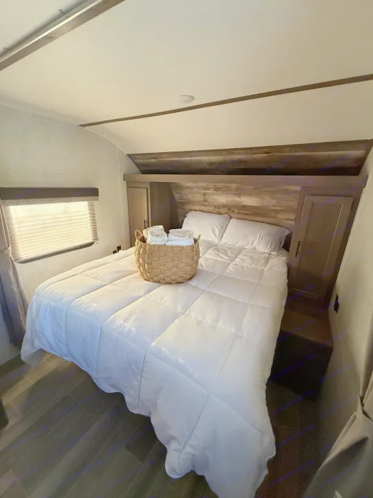 Cozy RV rental bedroom with a comfortable bed, white bedding, and a basket of fresh towels. Features modern wood accents.. Gulf Stream Ameri-Lite 2021