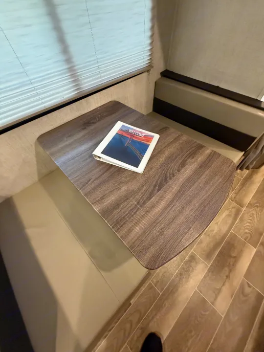 Cozy RV rental dinette featuring a wood table, comfortable bench seating, window with blinds, and a welcome binder for guests.. Gulf Stream Ameri-Lite 2021