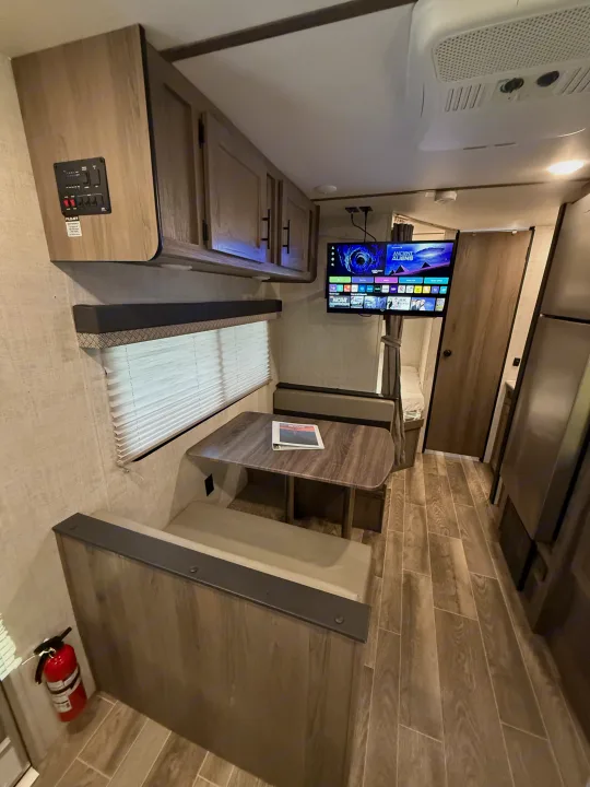 Inside this RV rental, a dinette with bench seating, a wall-mounted TV, and an overhead utility panel are visible. Wood-look floors.. Gulf Stream Ameri-Lite 2021