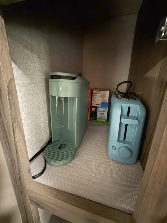 Compact kitchen essentials in an RV rental: a mint green Keurig, light blue toaster, and iced coffee pods, neatly arranged.. Gulf Stream Ameri-Lite 2021