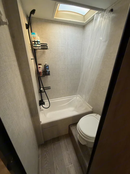 Compact RV rental bathroom features a tub/shower combo, toilet, skylight, and shower caddy with toiletries.. Gulf Stream Ameri-Lite 2021