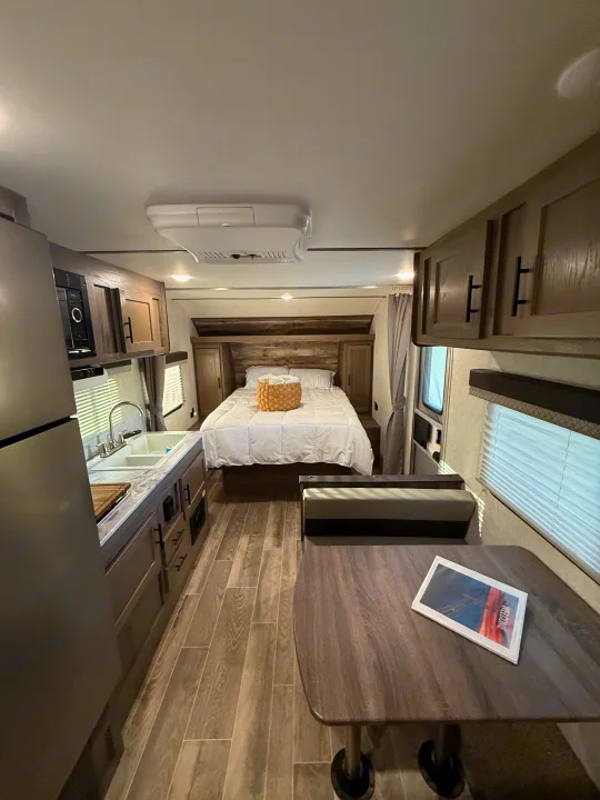 Bright RV rental interior: cozy bed, compact kitchen with sink, and a dinette area with seating and table.. Gulf Stream Ameri-Lite 2021