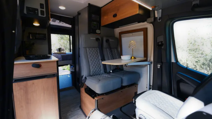 Modern RV rental interior with swiveling seats, a small table, kitchen, and a comfortable bed area in the back.. Mercedes Winnebago 2026