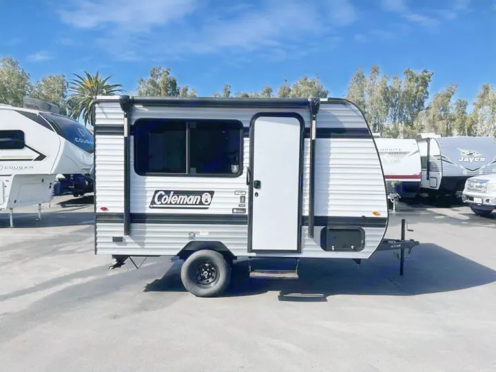 Coleman travel trailer, perfect for your next RV rental. This compact camper, with white and gray stripes, is ready for outdoor adventure.. Keystone RV Keystone Coleman 13R 2026
