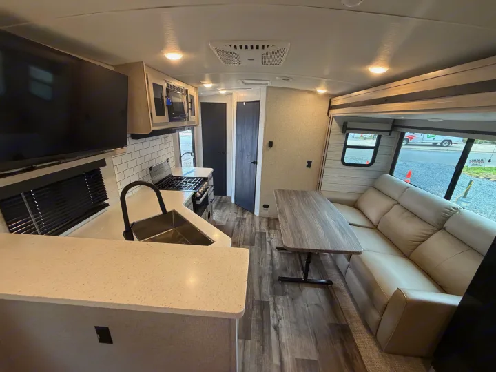 This modern RV rental interior showcases a bright kitchen with a sink, stove, dining area with table, and comfortable sofa seating.. Crossroads RV Sunset Trail Super Lite 2024