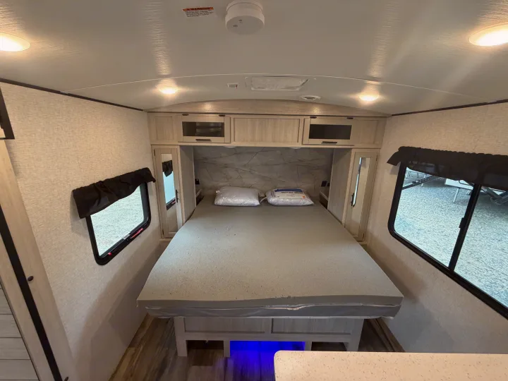 Interior of a clean rv rental bedroom with a comfy gray bed, mirrored closet, overhead storage, and windows for natural light.. Crossroads RV Sunset Trail Super Lite 2024